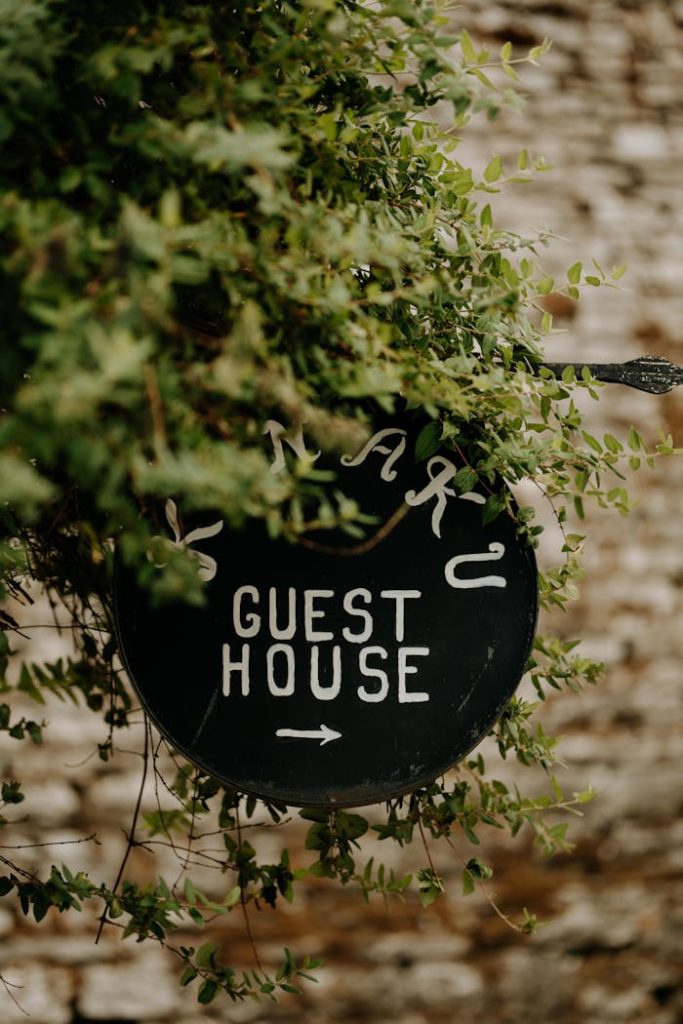 Rustic guest house sign surrounded by lush greenery on a brick wall backdrop.